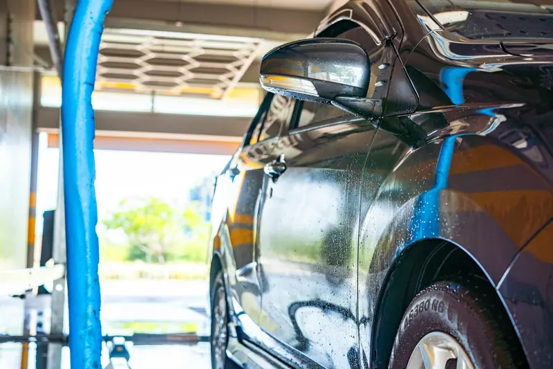 Wet car parked in a car wash bay beside a blue wash hose