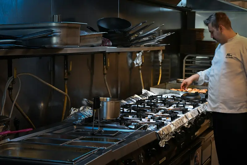 Chef at work on the line of a busy commercial kitchen with steel counters and burners