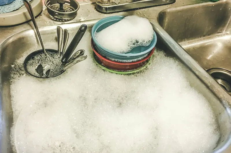 Dishes and spoons soaking in soapy water in a white kitchen sink