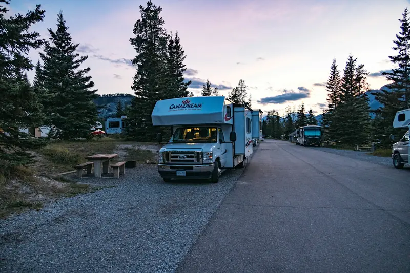 Motorhome parked at a campground at twilight with its lights on