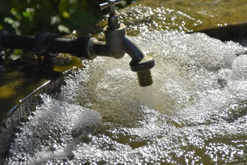 Outdoor tap pouring water into a basin of bubbling, foaming water