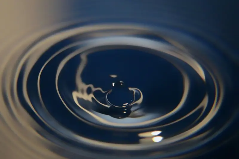 Single water drop striking a still surface and sending out rings of ripples